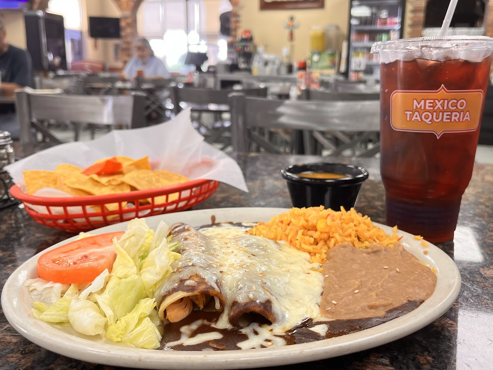 Cheese enchiladas plate with rice, beans, chips, and a Mexico Taqueria drink cup